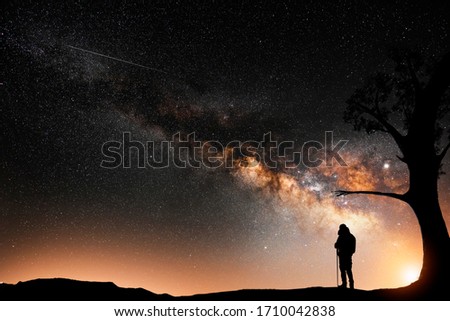 Man silhouette stands on the hill, behind him beautiful bright milky way galxy on the night sky.  
