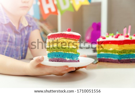 Kid celebrating birthday party and blowing candles on cake. Festive colorful birthday card with candles on rainbow cake and colorful balloons on background