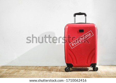 Red suitcase with inscription tag #stayhome against the background of a light wall in the room. Stay home, travel concept. Copy space. Royalty-Free Stock Photo #1710062416