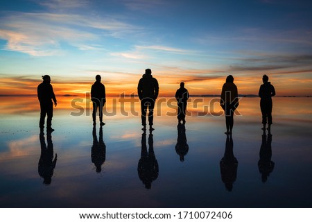 Diverse group of people against sunrise, silhouette of travellers at Uyuni Salt Flats (Spanish: Salar de Uyuni ) in Bolivia, South America, teamwork and leadership concept.