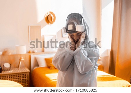Picture of an female in white chemical suit and gas mask at home in a large light room and doesn't know what to do because she is scared
