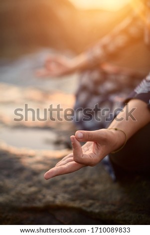 Beautiful curly woman by the ocean. Woman yoga hands with a sunset light. Breathtaking sunset. Ocean splashes. Amazing graceful woman doing yoga by the ocean sunset. Yoga poses.