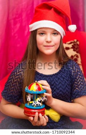 Girl in a blue elegant dress with Christmas toys in hands in a red armchair