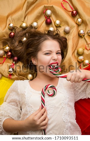 A girl in a white elegant dress with candy in her hands lies on a gold background