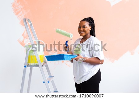 Happy African American woman painting wall in her new apartment. Renovation, redecoration and repair concept. Royalty-Free Stock Photo #1710096007