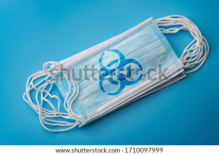 Respiratory sickness infection, novel coronavirus pandemic outbreak and sterile microbiology concept with surgical mask with biohazard logo isolated on blue background