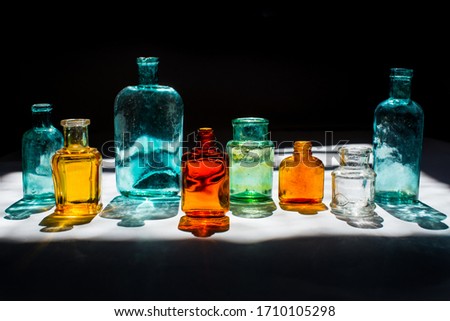 Colorful small glass bottles in sunlight on black background. Reflected light in the sun. Background glass. 