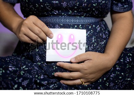 The pregnant woman uses the hand to hold the paper, with a smiley icon ahead of the concept of the happiness of the baby in the stomach.