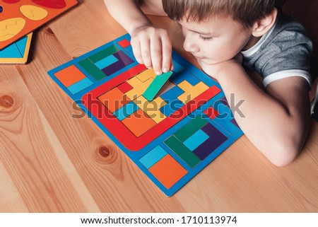Happy boy sits nearby desk and lays puzzles. the child puts the last detail in the solved puzzle.