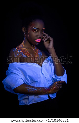 unusual fluorescent makeup on african woman's skin glowing under ultraviolet light. mysterious woman with UV painting on her body. body art