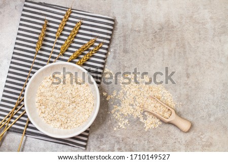 Oat flakes in a white ceramic bowl with a wooden spoon on a marble table in a top view