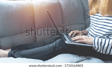 Women working from home or learning online education on laptop computer while sitting on the grey sofa at the living room in quarantine for Coronavirus or Covid-19.