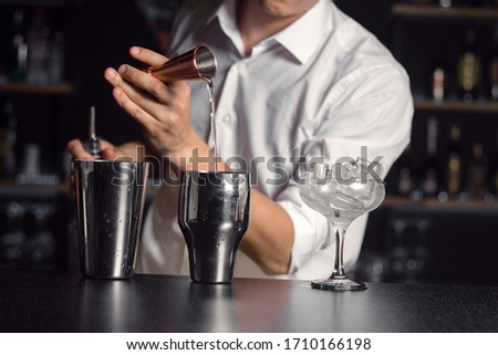 Cropped picture of hand of bartender dressed in white shirt. Glass vase with ice cubes on right side.Cocktail equipment on black shiny surface in focus.Horizontal layout