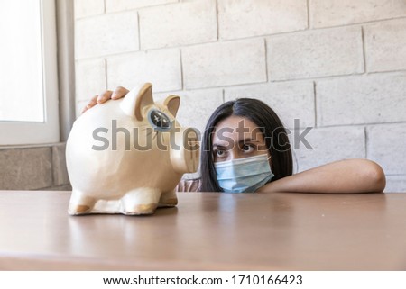 Young woman with face mask, worried face counting her savings in times of pandemic by COVID-19.