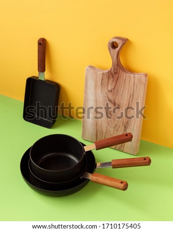 New frying pan set and wooden cutting board on colorful background. 
