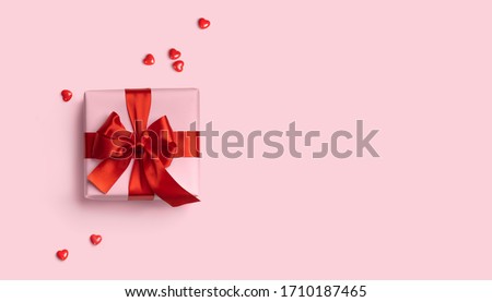 Pink gift box with red bow on pink background with red hearts. Holiday web banner. Top view.
