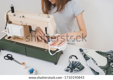Girl sewing protective medicine mask on sewing machine at home to prevent the flu. Covid-19 in the room with white background home workplace Royalty-Free Stock Photo #1710190843