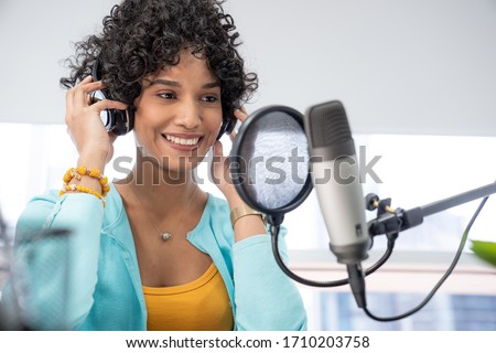 Good looking young black female making an online podcast recording for her online show. Attractive millennial African American business woman using headphones front of microphone for a radio program.