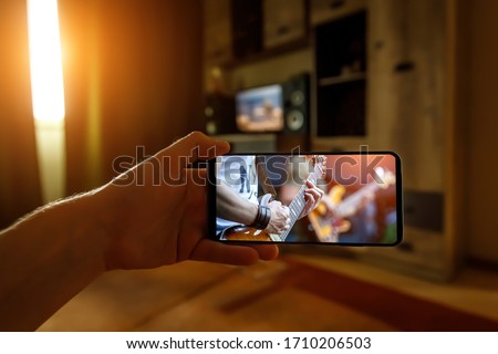 Watching online music concert at home using a mobile phone. Guitar close-up on the screen