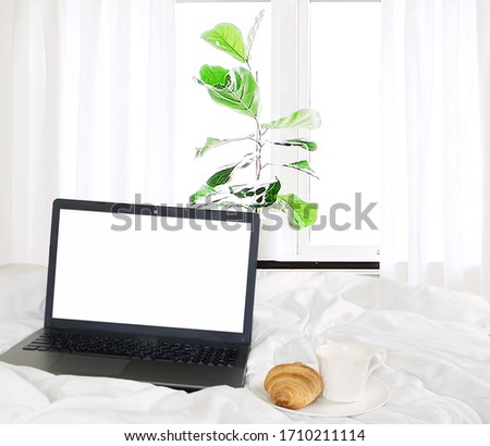 Selective focus,laptop,croissant and coffee in bedroom beside the window with a thin curtain and green trees blurred,relax and work online lifestyle from home concept
