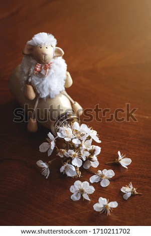 Funny sheep toy sitting on colorful bottle with flowers. Humor concept about spring