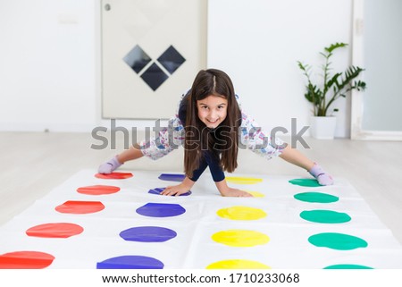 little girl playing on a twister game at home. Girl smiles and looks up