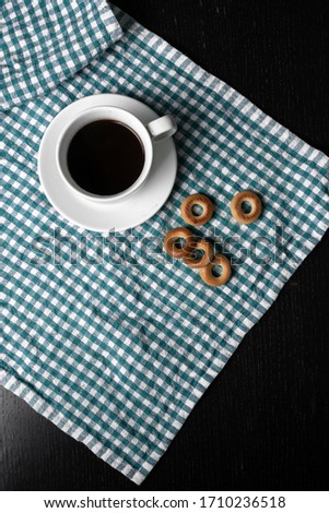a cup of black coffee with fresh crispy  bagels placed on a green white kitchen towel and on black background. 
