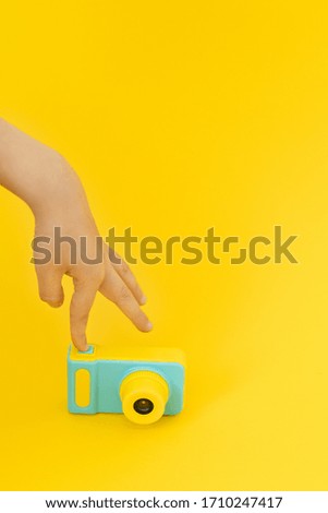 Hand turns on little kids photocamera on yellow background.