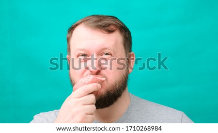 A fat chubby man with a beard eats sausage or meat, a concept of harmful unhealthy lifestyle