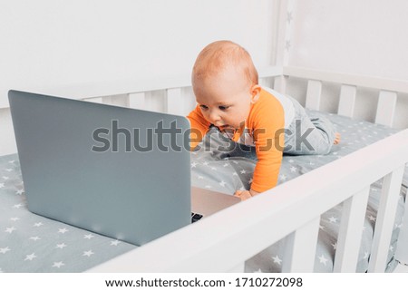 Baby lying on the bed with interest looks at the laptop screen. New generation.