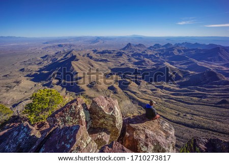 Man Sitting On Edge Of Cliff Overlooking Desert Landscape - Chisos Mountains South Rim, Big Bend National Park, Texas Royalty-Free Stock Photo #1710273817