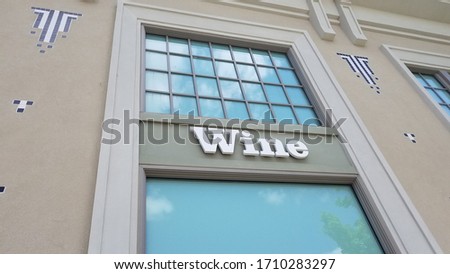Store window wall sign advertisement that spells the word wine. Has a mild sky blue reflection in the window. 