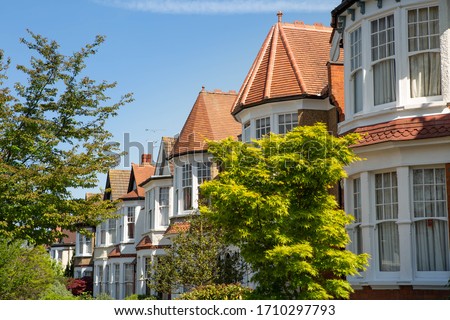 Lovely English Edwardian residential houses in a row with spectacular wooden bay casement windows. Front view on the properties from the street with green trees on a sunny day. London, UK 21/04/2020 Royalty-Free Stock Photo #1710297793