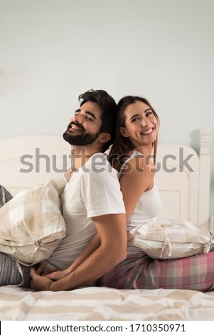 Cheerful couple having fun while sitting back to back in their bedroom