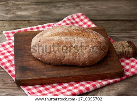 baked round rye flour bread on a kitchen cutting board, top view