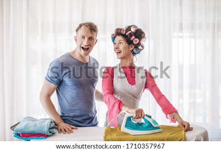 Young couple at home doing household chores and ironing. Wife ironing clothes for her husband at work, emotional photo of a married couple. Concept on the subject of iron. Lifestyle. Honeymoon. Life.
