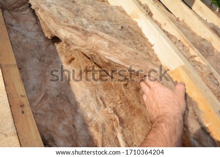 A bad example, mistake of a building contractor applying thermal mineral, glass wool batt insulation without protective gloves under the roof sheathing, between trusses constructing the roof. Royalty-Free Stock Photo #1710364204