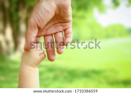 Father holds the hand of a small child in the park on the nature vacation background
