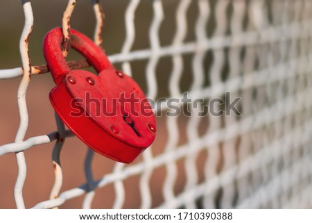The red padlock hanging in the fence of the bridge