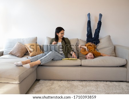 Mirthful lady working online in the quarantine and her child playing while getting bored at home stock photo