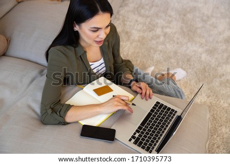 Attractive lady sitting by the couch with notebook, gold card and smartphone stock photo