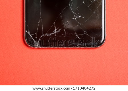 Black mobile phone or tablet with a broken screen. Smartphone on a red background close-up. Broken screen glass.