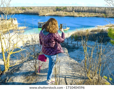 Hiker on mountain top with smartphone. Woman is standing and taking a picture on smartphone. Abandoned Quarry Of Rummu, Estonia. Scenic View Of Land Against Clear Blue Sky. Panoramic View. 