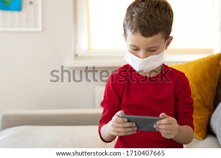Littke child is sitting on sofa and spending time with gadget stock photo. Website banner. Stay at home concept