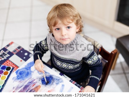 Lovely toddler boy having fun indoor, painting with different paints colors