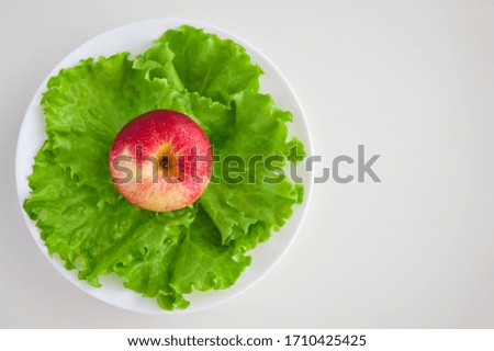 red apple and lettuce salad on a plate on a white table