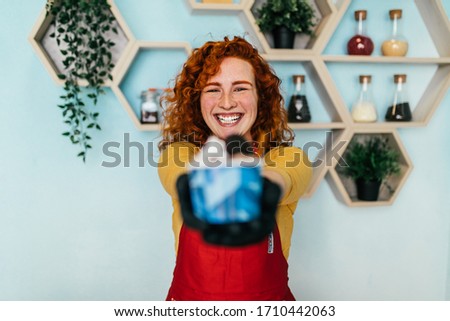 Beautiful and positive redhead ginger woman smiling and working in handmade ice cream store. She preparing and serving delicious sweet food.