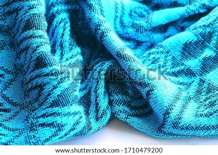 Knitted turquoise-coloured fabric with soft folds and with a geometric drawing view from the top in light from the window. Copy space