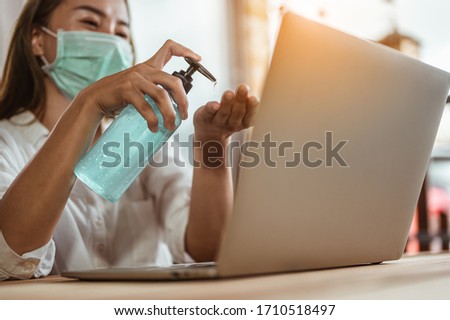 Office worker working from home during coronavirus outbreak cleaning her hands with sanitizer gel and wearing protective mask. Coronavirus, covid-19, Work from home (WFH), Social distancing concept. Royalty-Free Stock Photo #1710518497