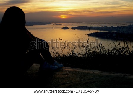 Woman resting on the sunset at Niteroi and Rio de Janeiro cities, Brazil. View of tourist spots in the cities, such as Guanabara Bay                                           